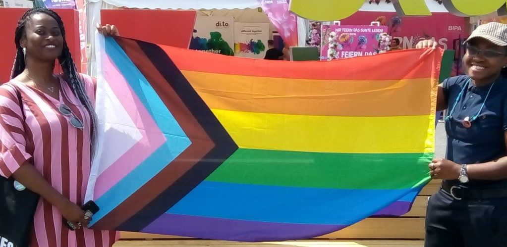 Two people at EuroPride 2019 Vienna holding an LGBTQ pride rainbow flag featuring a design by Daniel Quasar