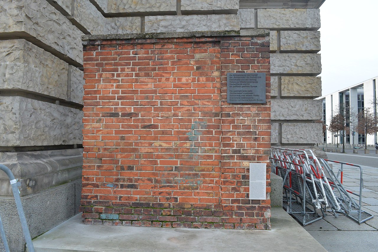 Section of a brick wall from the Gdańsk Shipyard in Gdańsk, Poland, standing against the northwest corner of the Reichstag Building in Berlin by Jjjjjjjjcross